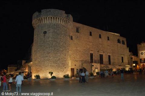 Conversano castle at night, illuminated round stone tower, people strolling in the square