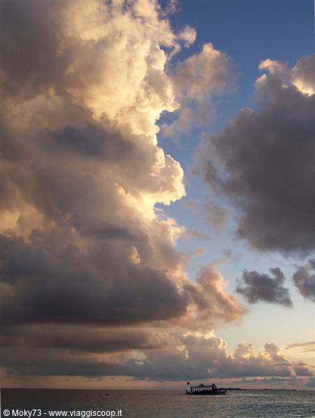 Sunlit clouds over calm sea, a small boat silhouetted on the horizon