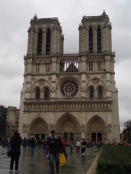Tourists on wet square in front of Notre-Dame's Gothic facade under grey sky