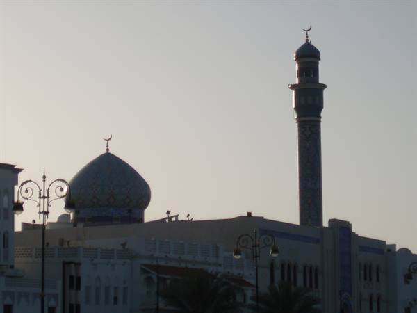 Minaret and blue mosque dome rising above white buildings, backlit