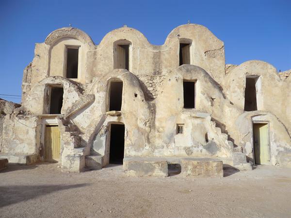 Earthen ksar with stacked ghorfas, external stairs and blue sky, Medenine