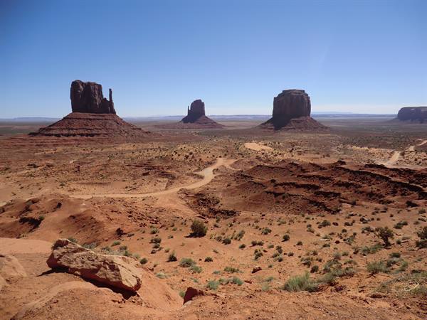 Monument Valley: red sandstone buttes over sandy desert shrubs, blue sky