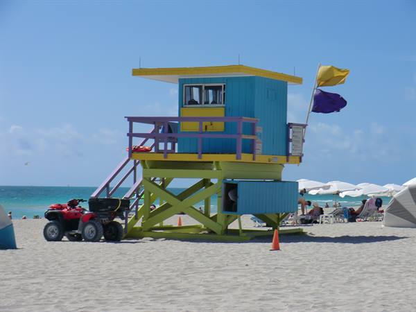 Lifeguard tower on sandy beach, red quad bike nearby, umbrellas and tourists