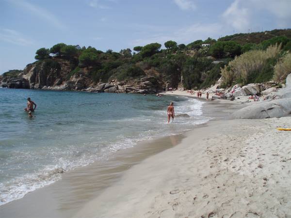 Swimmers on pale sand beach, rocks and green hillside in the background