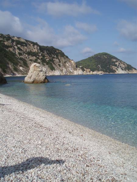 white pebble beach, rock and green hills over turquoise water