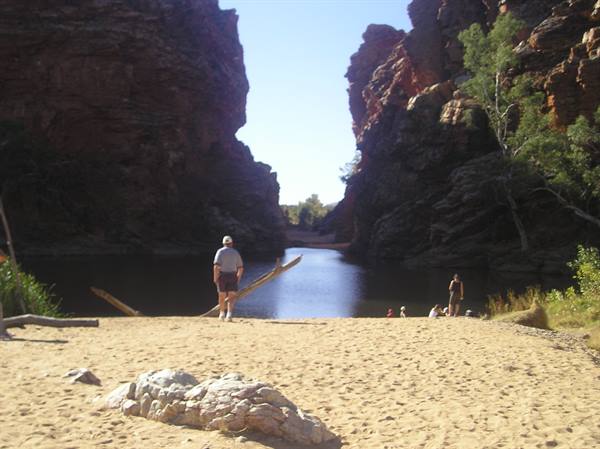 Tourist in hat on red sand before a gorge with a waterhole