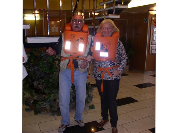 Elderly couple smiling in orange life jackets inside the ship's lobby