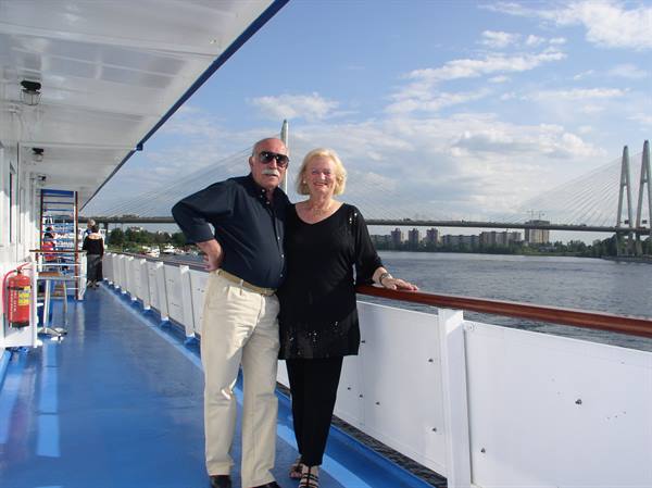 Couple posing on ship deck, cable-stayed bridge over river behind