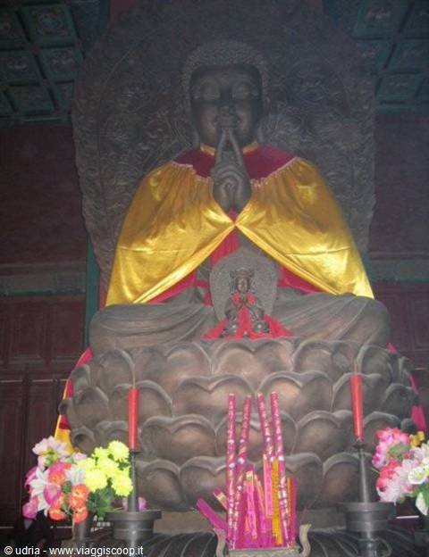 Large bronze Buddha statue draped in yellow cloth, incense sticks and flowers, temple