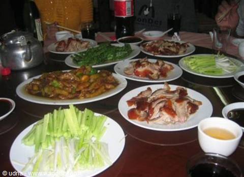 Round table with Chinese dishes, duck and vegetables, tea and bottles