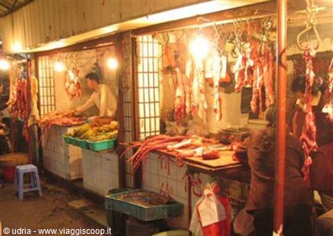 Covered market with meat stalls, hanging cuts lit by bare bulbs