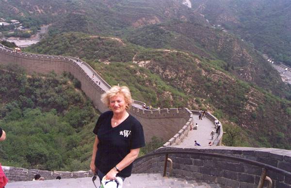 Blonde woman stands on Great Wall steps among green hills