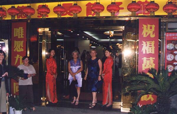 Women in dark dresses with two hostesses in red qipao at a lantern-lit Chinese restaurant entrance