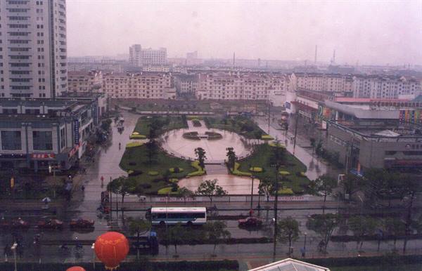 City square with green flowerbeds and fountain after rain, bus and tower