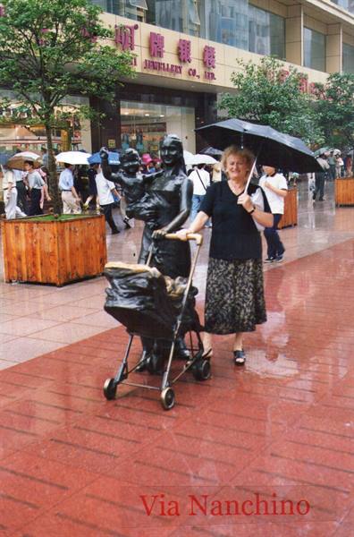 Woman with black umbrella next to a bronze statue, wet pavement