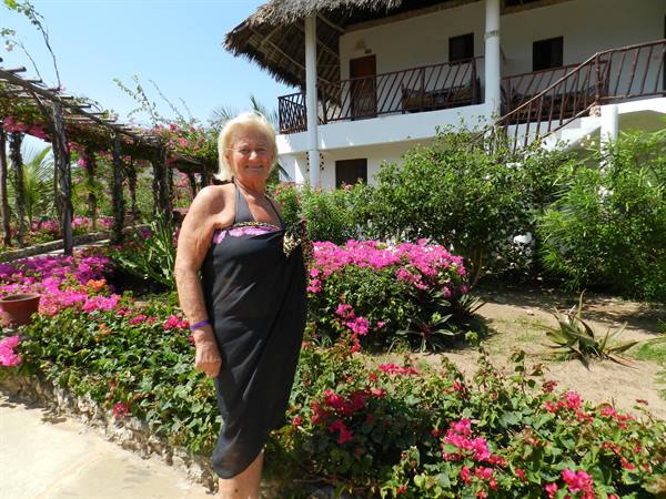 Blonde woman in black sarong among blooming bougainvillea in front of thatched-roof resort
