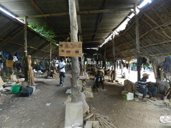 Carvers working under open wooden shelter with thatch and tin roof