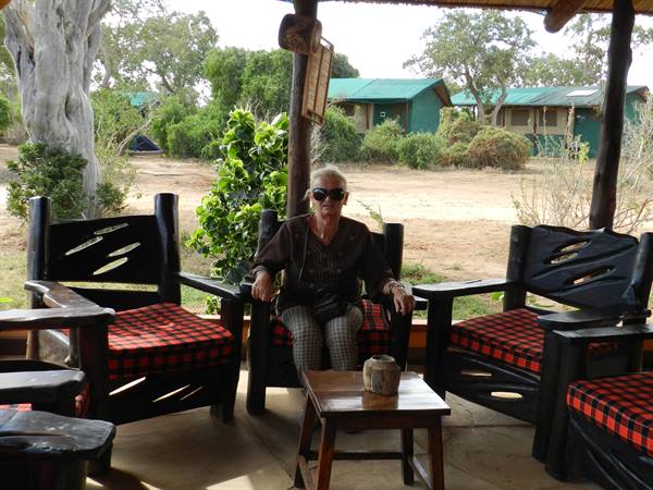 Woman in sunglasses sitting on carved wooden armchair with tartan cushions