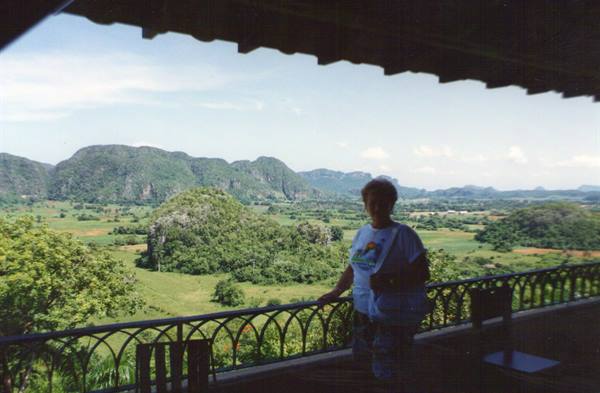 Woman in white t-shirt on wrought-iron terrace overlooking lush Vinales valley