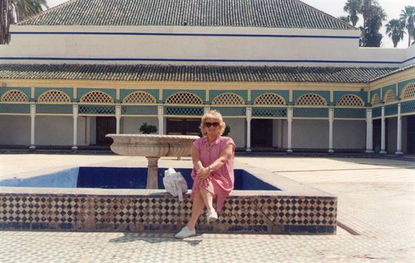 Woman in pink dress sitting on a fountain in Marrakech Bahia courtyard