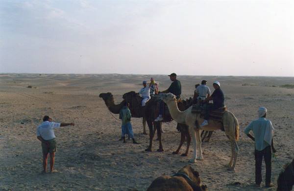 Tourists riding camels on the sand, guide pointing the way