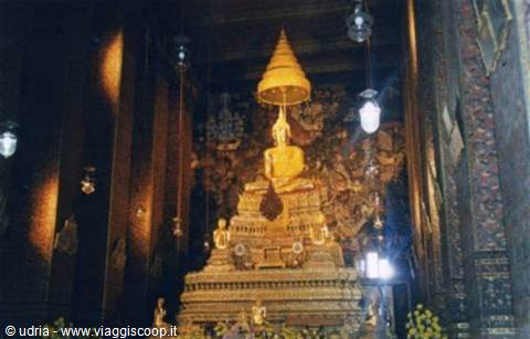 Golden Buddha under parasol inside Wat Pho temple, lamps and offerings