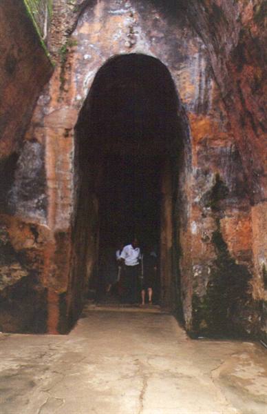 Visitors entering a dark ancient stone archway, moss-covered walls