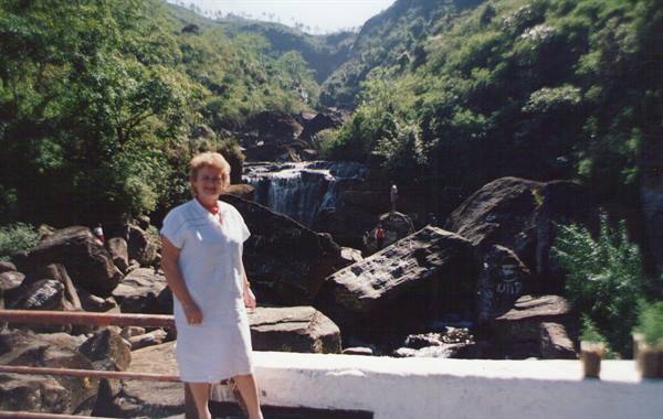 Woman in white beside waterfalls among rocks and lush greenery