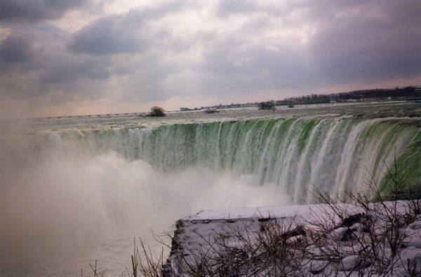 Snowy Niagara Falls, green water cascading amid mist and cloudy sky