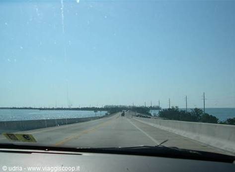 Driving across a long ocean bridge toward green islets, dashboard visible, sunny sky