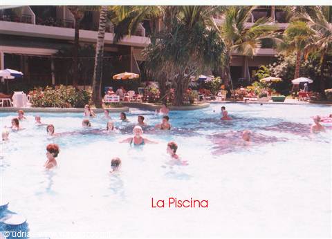 Tourists swim in the hotel pool among palm trees and colorful umbrellas