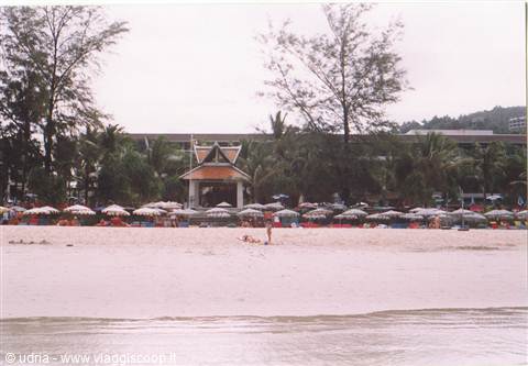 Beach with umbrellas and wooden pavilion, trees and hotel in background