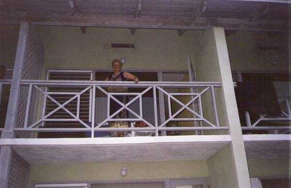 Woman standing on hotel balcony, white cross-pattern railing, wooden beams