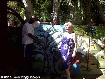 Two people beside a painted mural of a tree and houses among palms