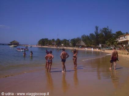 Tourists in swimsuits on golden sand beach, thatched umbrellas and boats along the coast