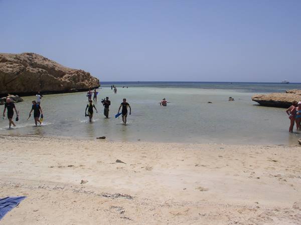Snorkelers wading in shallow turquoise water between rocky cliffs on sandy beach