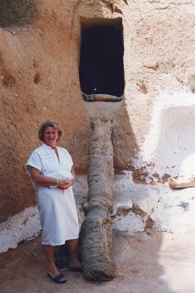 Woman in white dress beside palm trunk under a window carved in rock
