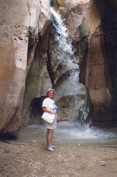 Woman in white beside the Ein Gedi waterfall among limestone rocks