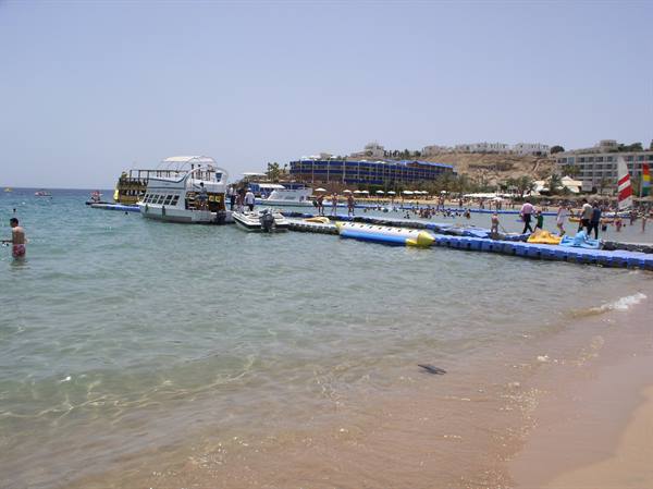 White boats moored at blue floating pier, tourists on sandy beach