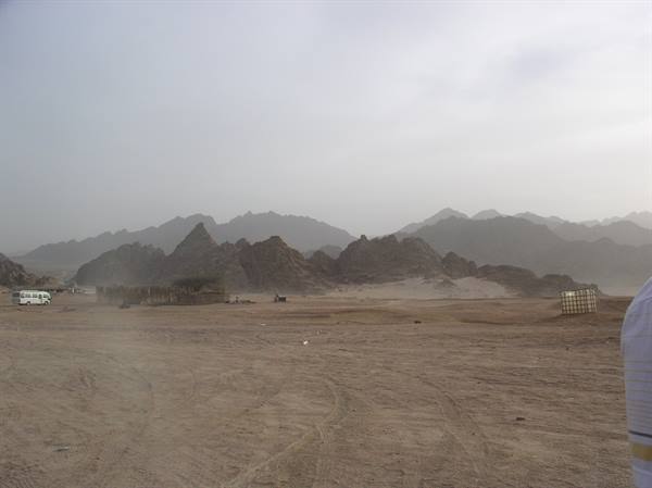 Bus parked on desert sand, rocky mountains fading into haze