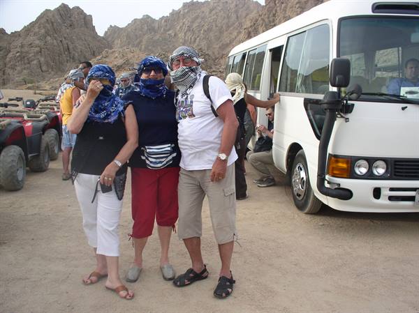 Tourists wearing keffiyehs beside a white bus in rocky desert