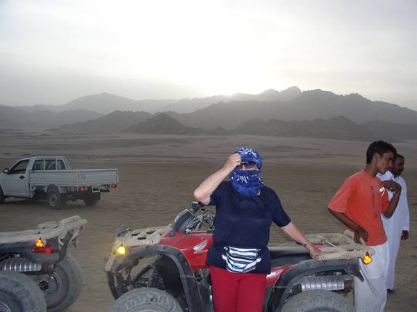 Tourist in blue headscarf beside a red quad bike in the desert, hazy mountains
