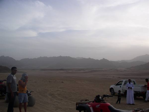 Tourists and guide in robe beside quad bikes in rocky desert