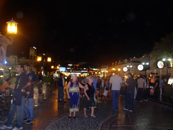 Tourists stroll at night past glowing lanterns and signs in Sharm el-Sheikh pedestrian street