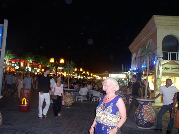 Blonde woman in embroidered blue dress walking on illuminated street at night