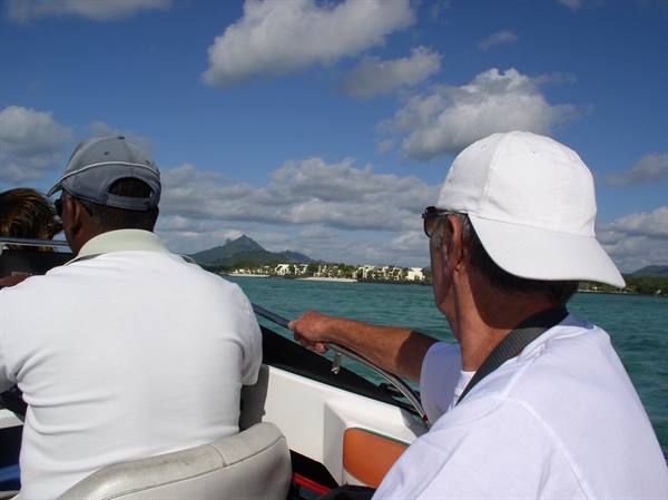 Two men on a boat gaze at the turquoise coast with volcanic mountain behind