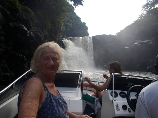 Tourist on a boat in front of a large waterfall among dark rocks