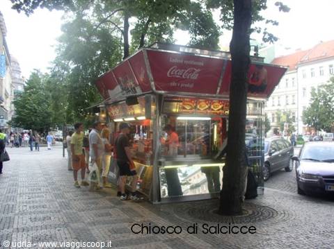Sausage stand of glass and steel, customers queueing under trees