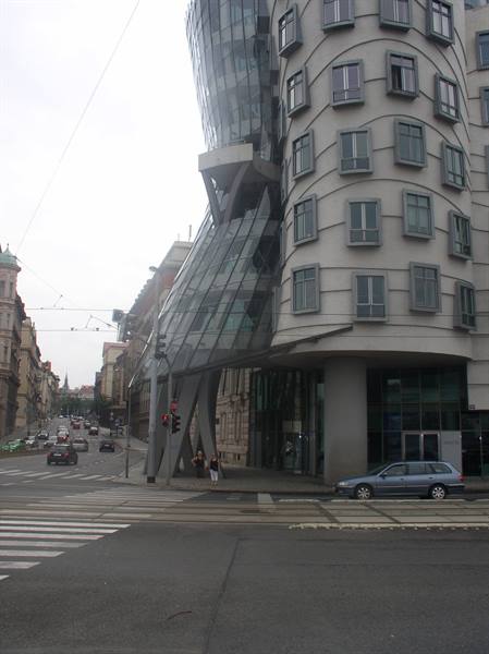 Prague's Dancing House with curved glass facade, cars and pedestrians crossing