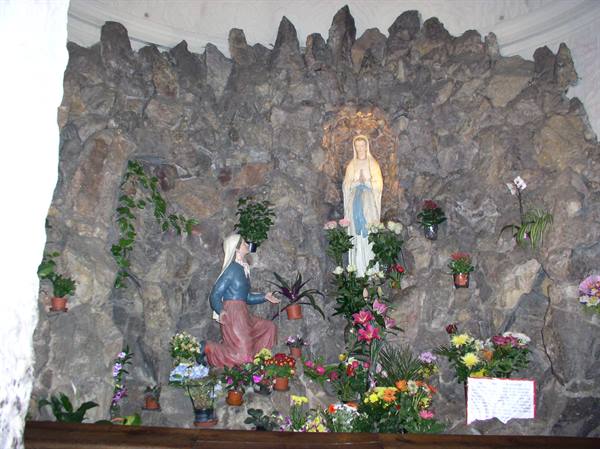 Our Lady of Lourdes statue in rock grotto with flowers and Bernadette